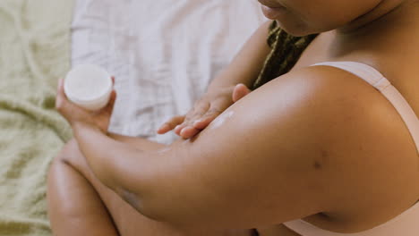 top view of woman in underwear sitting on the bed spreading moisturizing cream on her arms