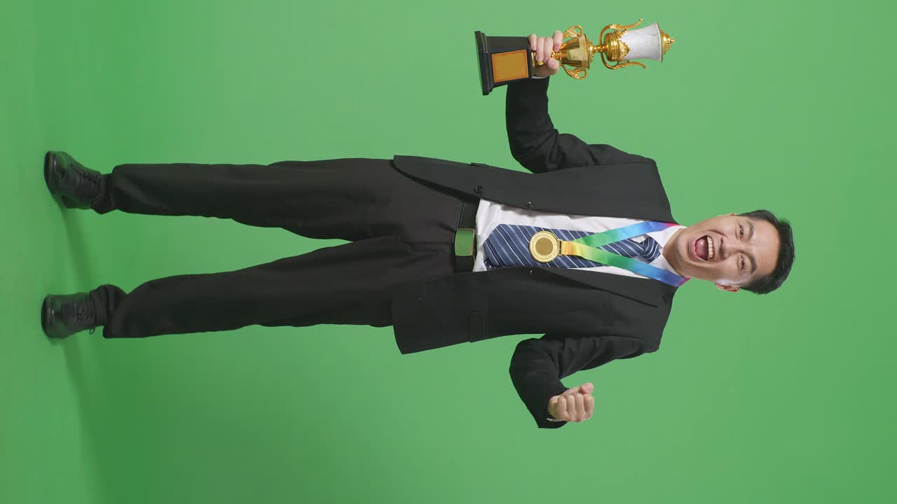 슈트와 타이를 입은 아시아 사업가, 금메달과 트로피를 들고, 골을 치며 우승을 축하하는 첫 번째 우승자, 스튜디오의 녹색 스크린 배경