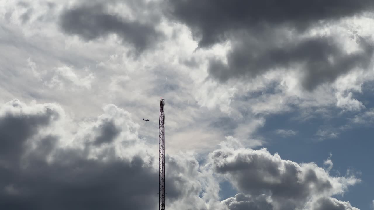 Clouds hover over a tall radio tower under a dramatic sky with plane