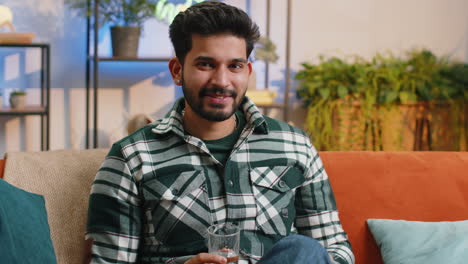 Thirsty-indian-man-sitting-at-home-holding-glass-of-natural-aqua-make-sips-drinking-still-water