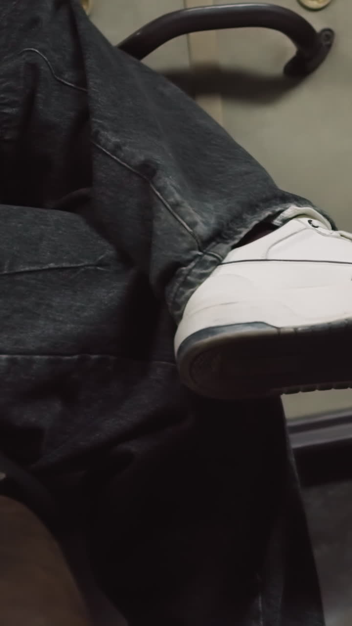 vista de primer plano de una persona sentada en un coche con las piernas cruzadas, sosteniendo un teléfono inteligente, con un atuendo casual, zapatillas blancas, y el acogedor