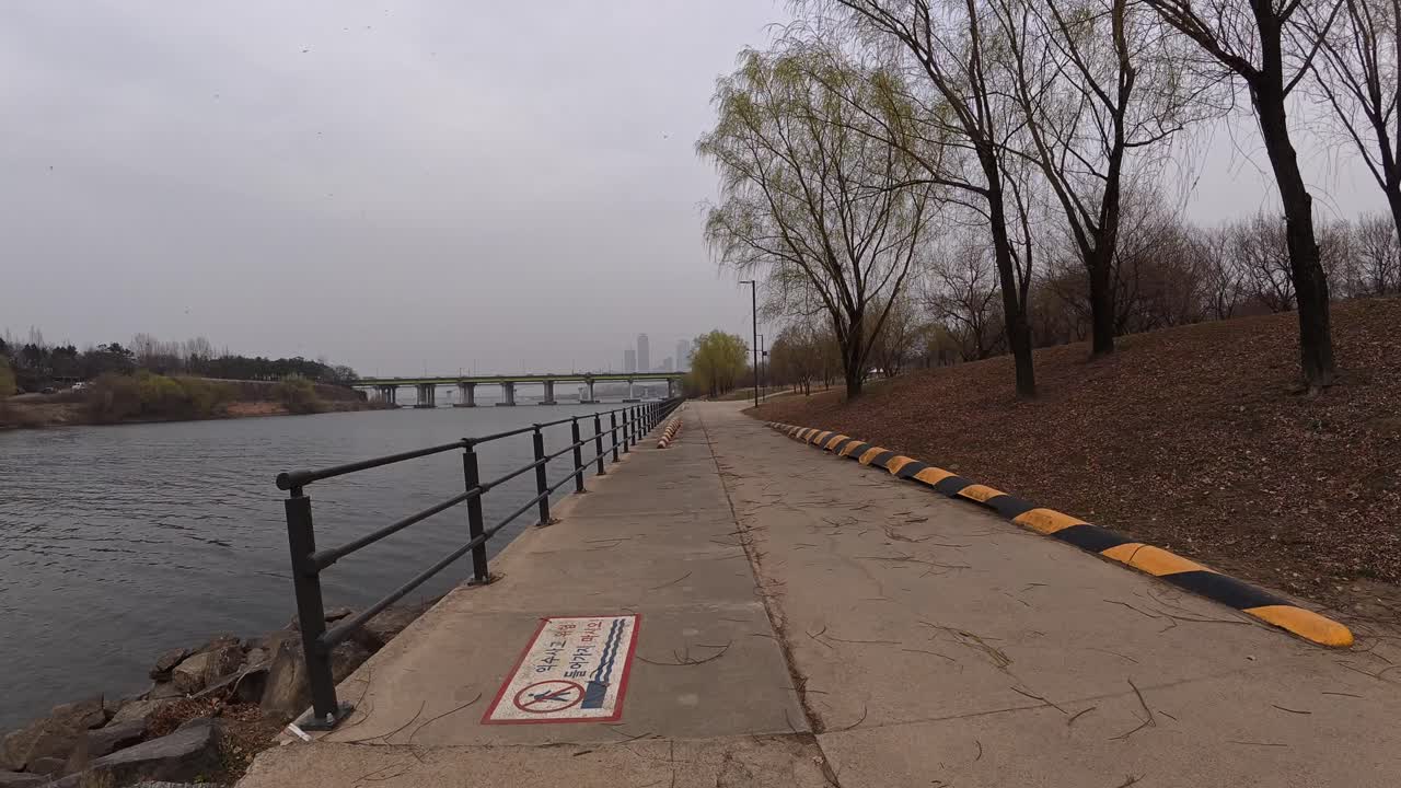 Walkway At Riverside Park With Bare Trees With Yanghwa Bridge In Distance. Han River In Seoul, South Korea. wide POV shot