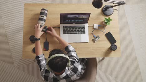 top view of a male editor with headphone putting the memory card on a laptop then choosing the video in the workspace at home