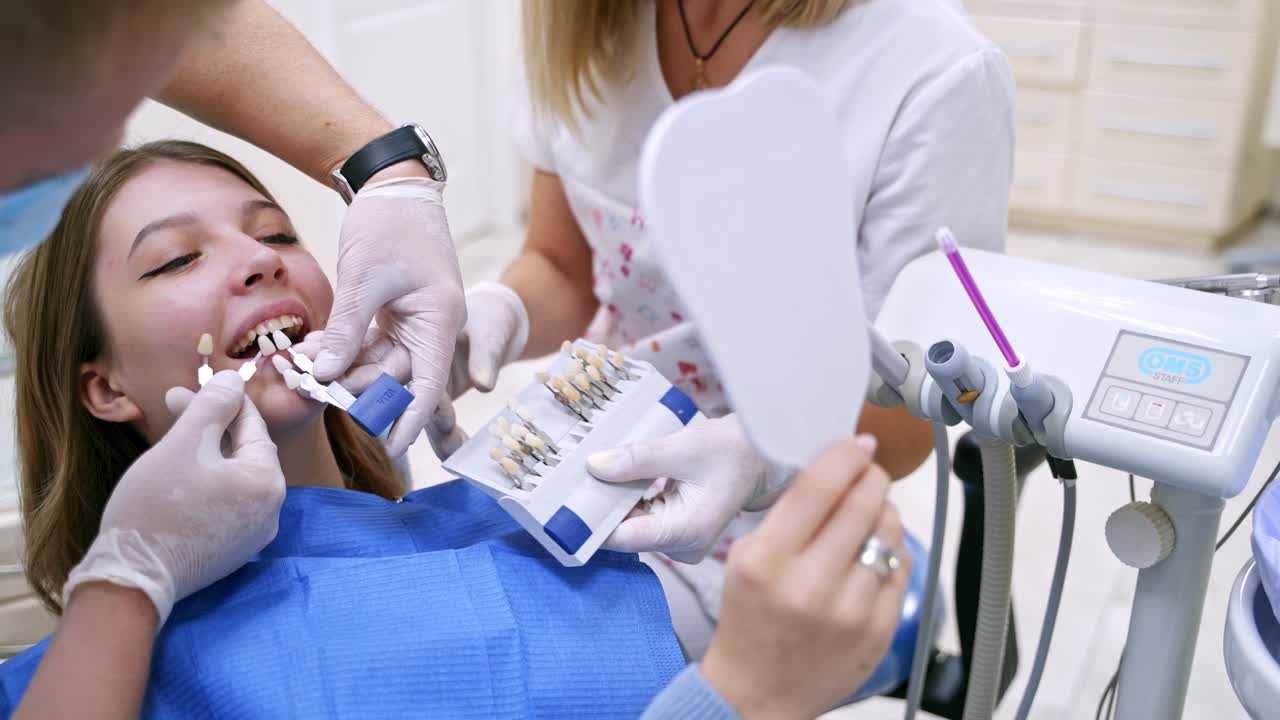 Dentist holding artificial tooth close to patient's teeth. Dentist with assistant select a color of tooth for the patient. Progress of dental implantology.