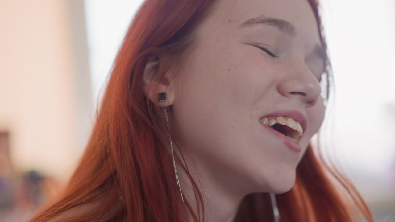 Donna con auricolari che canta gioiosamente. Giovane donna con lentiggini che canta dolcemente alla luce naturale. Vocalist femminile rilassata con lentiggini che canta un brano indie in un'accogliente camera da letto