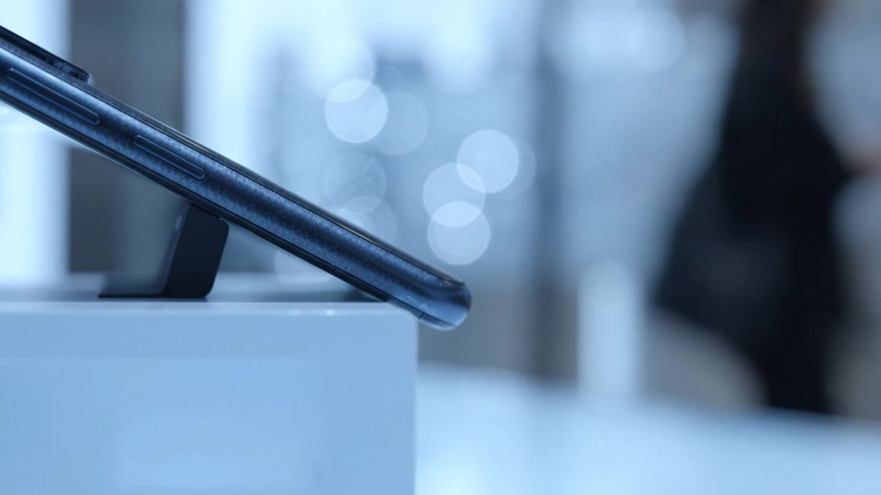 Nærbilde av en moderne smarttelefon elegant utstilt på et stativ i en stilig, uskarp bakgrunn, som fremhever enhetens elegante design og teknologiske funksjoner.