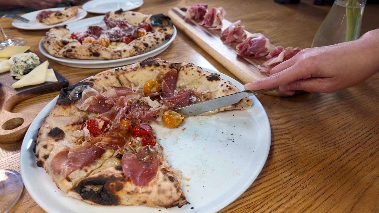 Vista dall'alto di mani che tagliano pizza artigianale e servono fette su un tavolo di legno