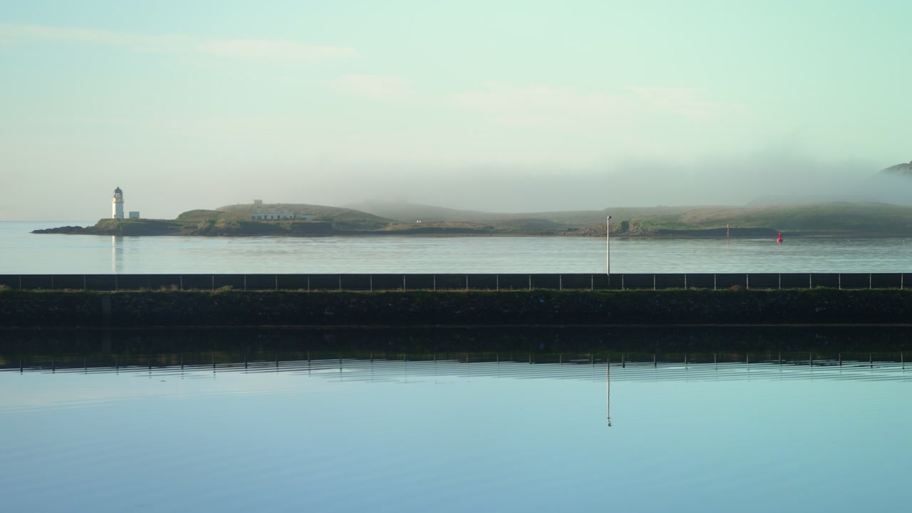 Static shot of morning mist rolling over Stornoway lighthouse in summer.