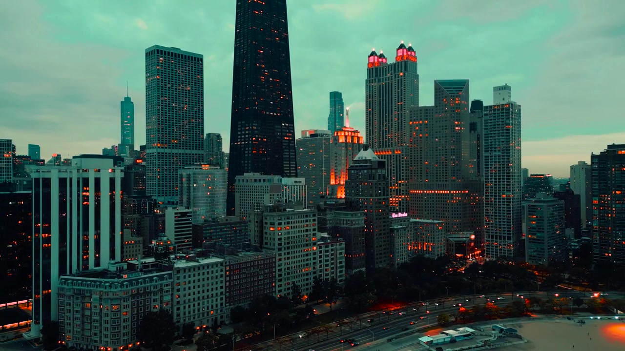 Una ripresa aerea cinematografica del centro di Chicago al crepuscolo, che cattura lo skyline illuminato della città, le finestre luminose dei grattacieli e la suggestiva atmosfera serale. La scena mette in risalto il contrasto tra