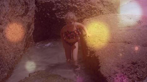 puntos de luz contra la chica caucásica caminando cerca de las rocas cerca del mar