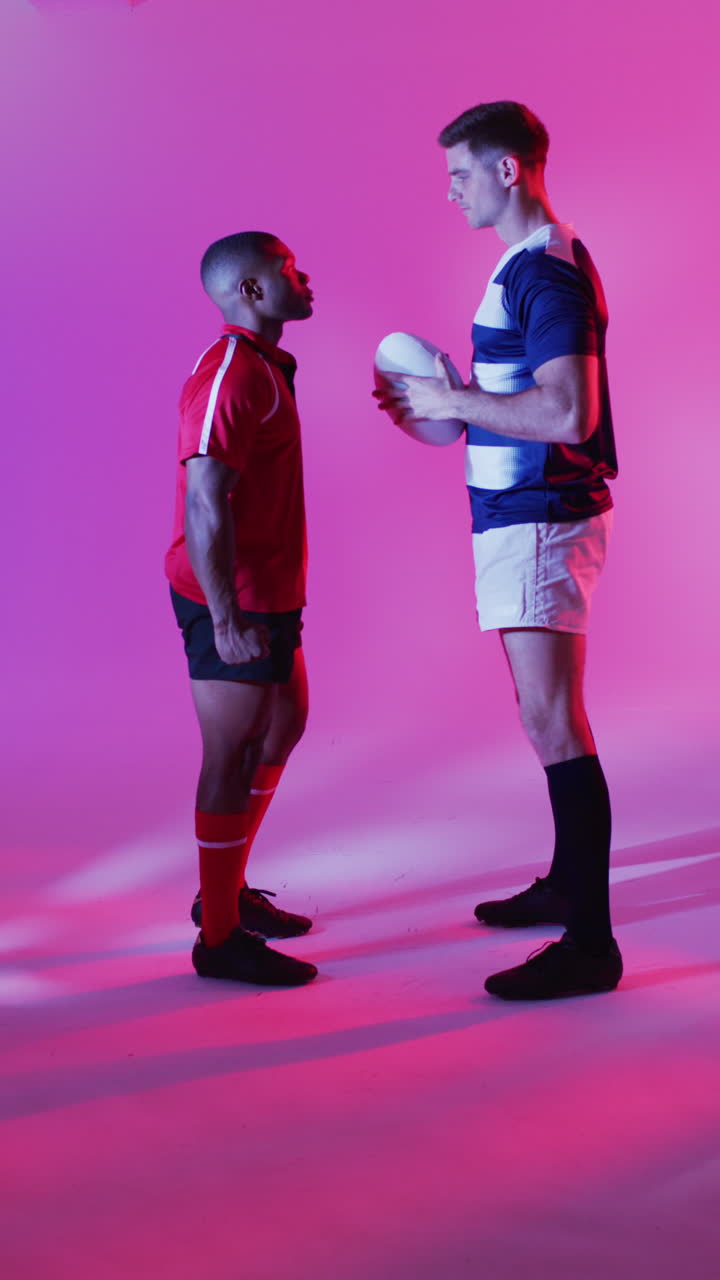 video vertical de diversos jugadores de rugby masculinos con una pelota de rugby sobre iluminación rosada