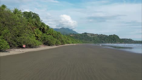 flying close to the wet sand in costa rica beach during low tide with mountains in the background