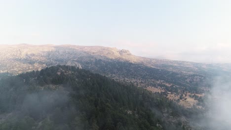 Aerial-backward-view-of-a-valley-and-its-surrounding-mountains-with-mist