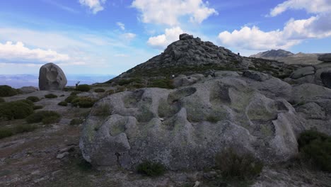 Seitlicher-Flug-In-Einem-Bereich-Mit-Heiligen-Felsen-Im-Hintergrund-Befindet-Sich-Ein-Monumentaler-Mit-Seinem-Erklärenden-Schild-Und-Im-Vordergrund-Sehen-Wir-Einen-Mit-Vielen-Schalen,-Die-Für-Rituale-Und-Opfergaben-Verwendet-Werden