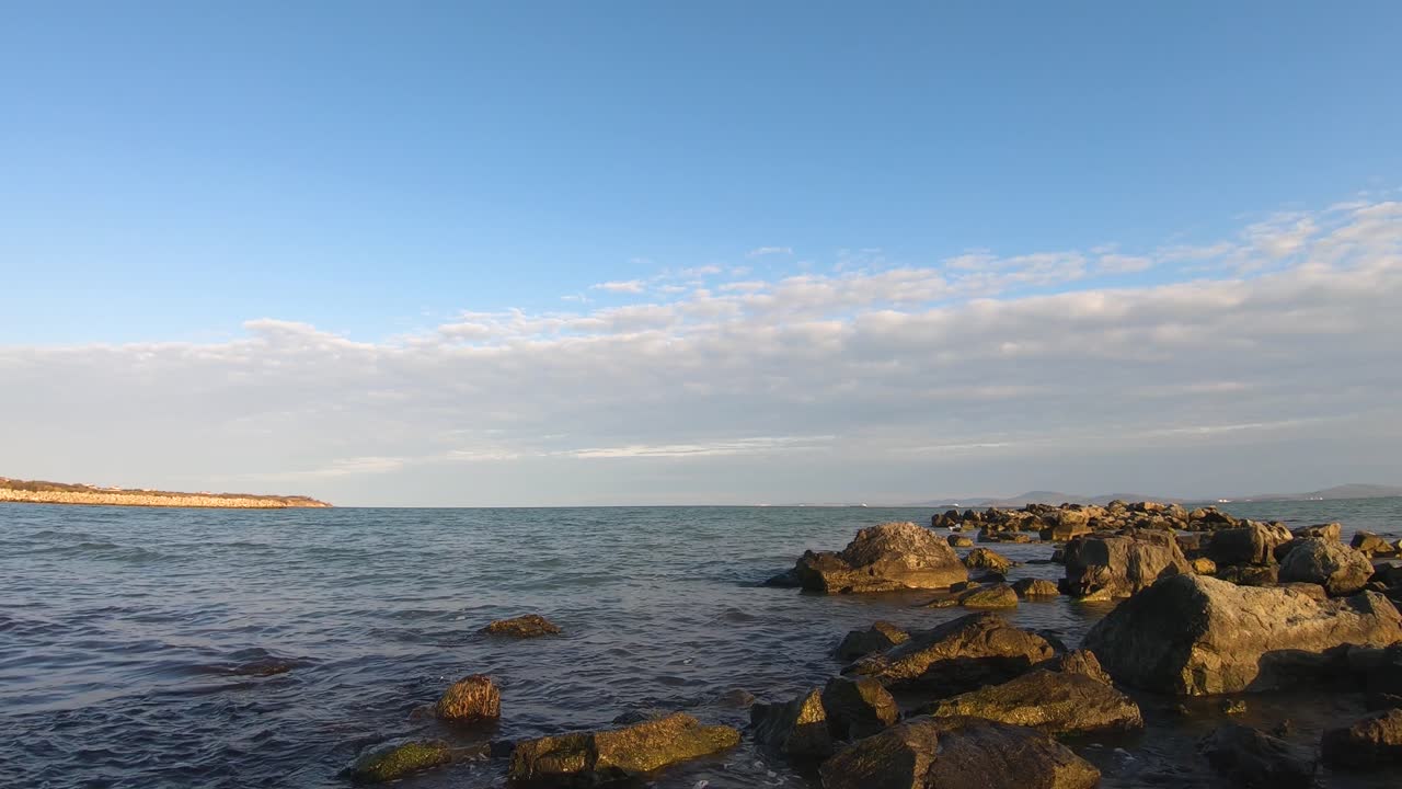 Time lapse from sea rocks in bay. View to the calm sea and cape. Cloudscape with altocumulus clouds. Small waves in summer day