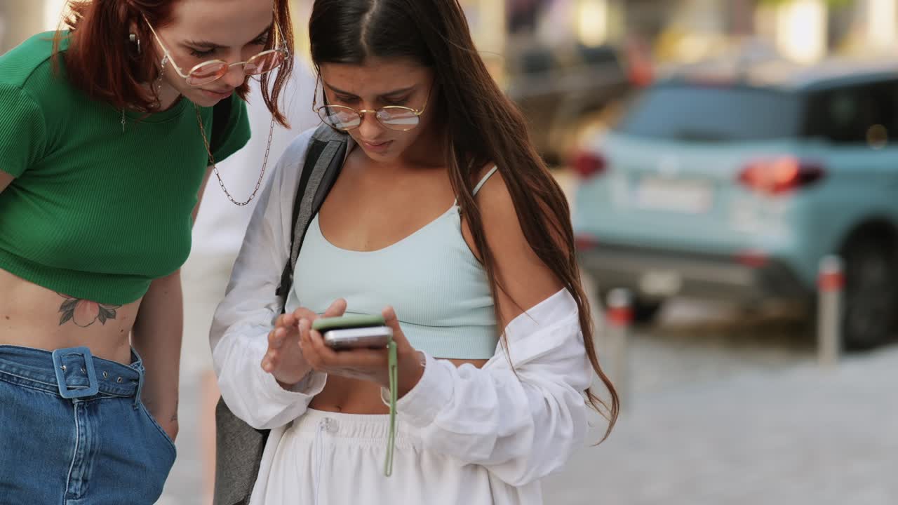 dos mujeres jóvenes mirando un teléfono inteligente al aire libre
