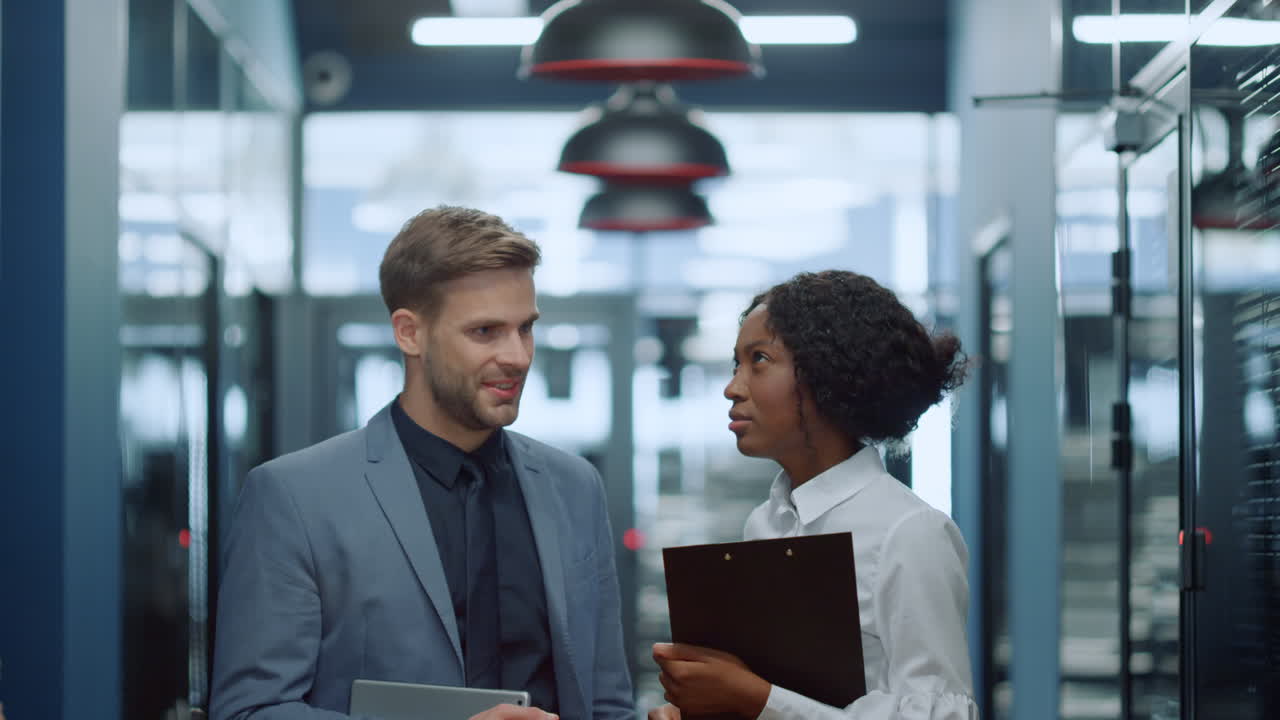 Multiracial couple having discussion in corridor. Colleagues waiting for meetup
