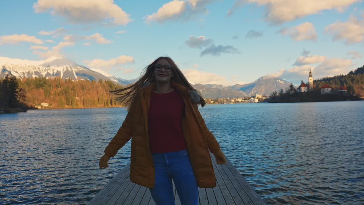 video en 4k de una hermosa y feliz joven caucásica caminando por el muelle en un destino turístico muy famoso, bled, eslovenia.