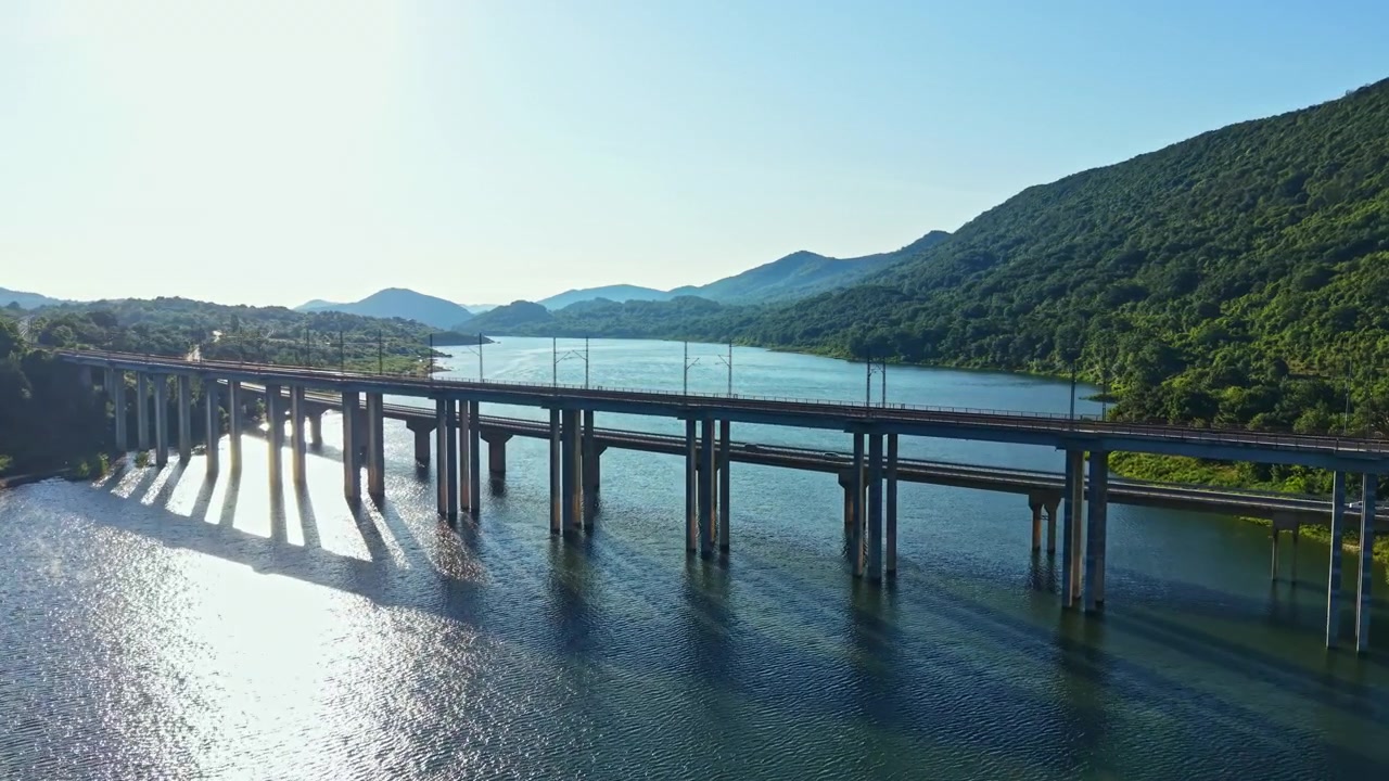 日中、澄み切った空の下、水面を渡る橋。背景には山々がそびえる。