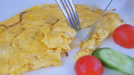 close-up of a fork cutting into an omelette with tomatoes and cucumber on a white plate