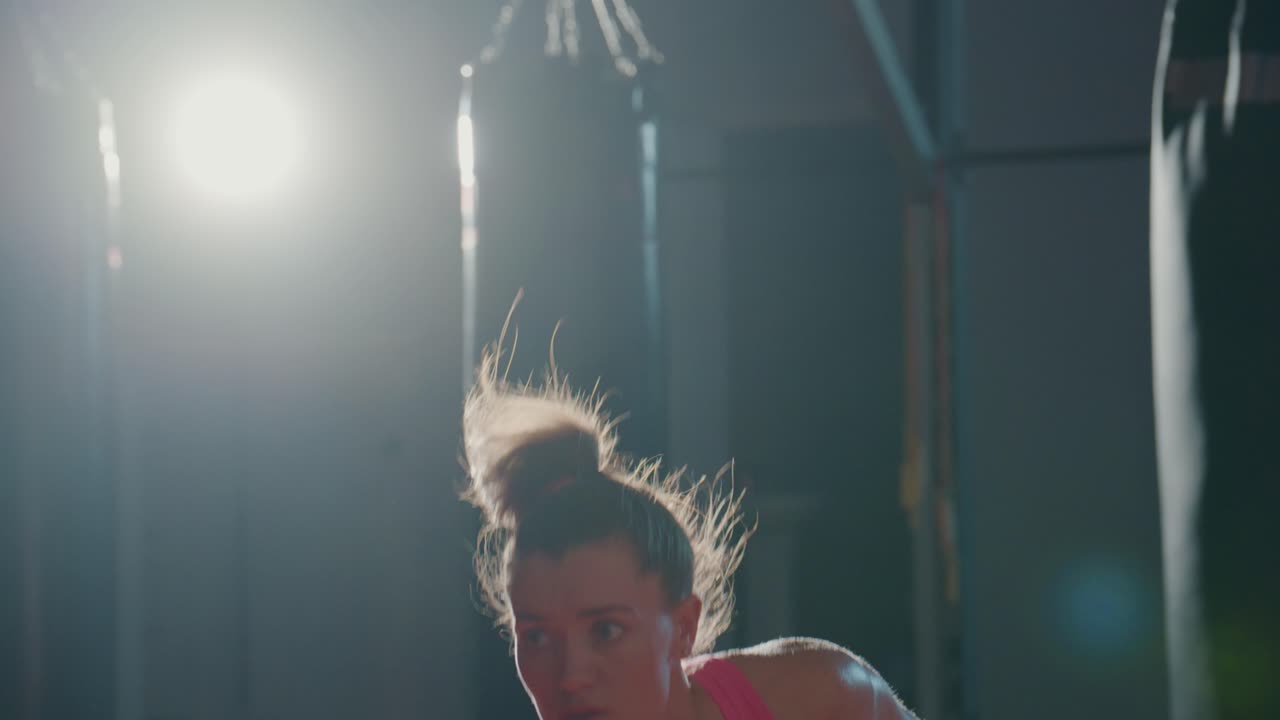 Donna determinata che solleva un manubrio sopra la testa in una palestra buia.