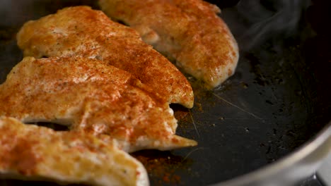 close-up slow motion shot of garnish paprika pepper on chicken cooking in fry pan on stove cooktop kitchen hospitality health food 4k