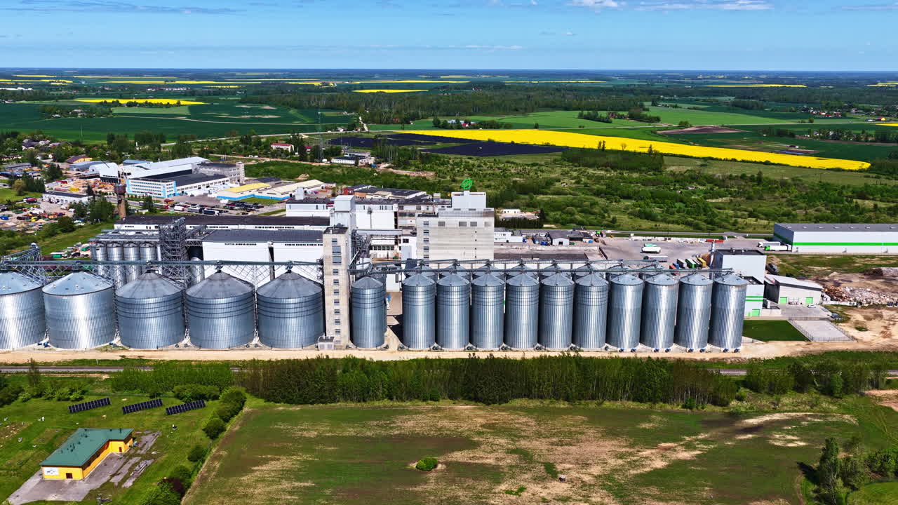 Large grain silos next to a modern processing plant in flat green farmland