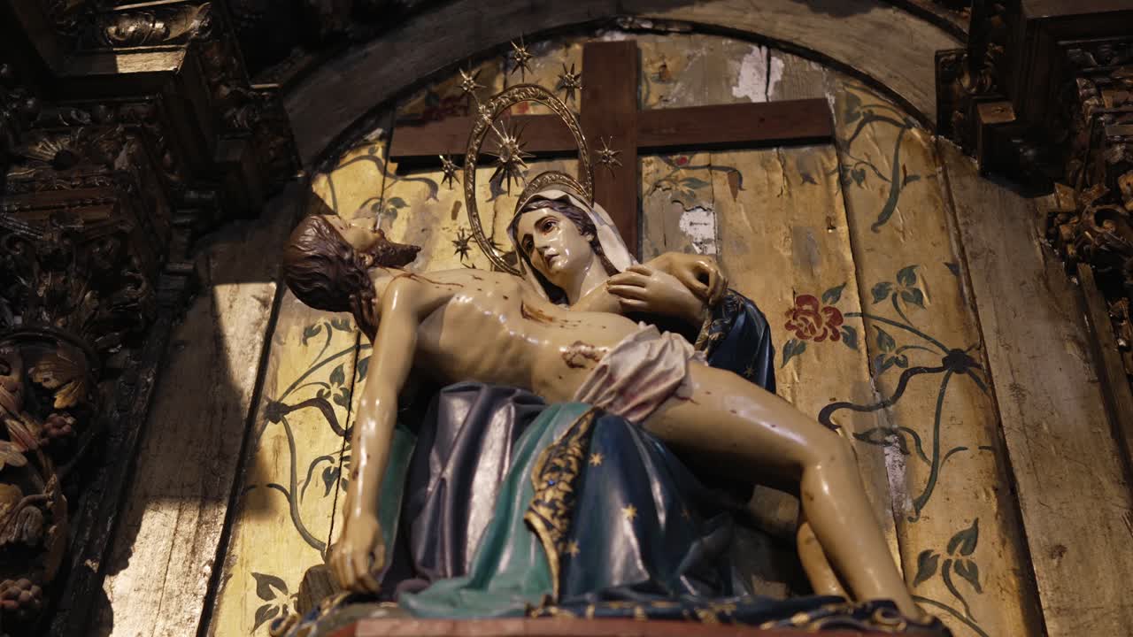 Sculpture of the Virgin Mary holding the body of Christ, set against golden floral backdrop