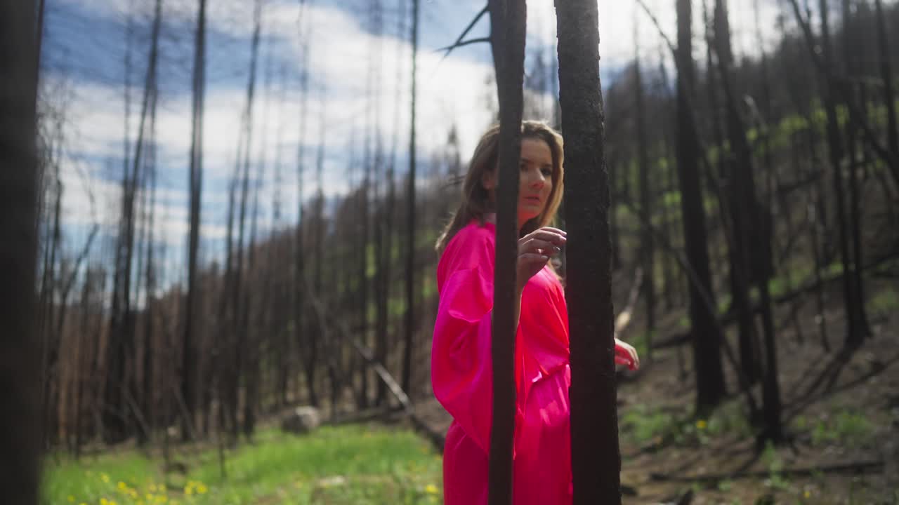 темноволосая девушка в розовом халате проходит через деревья.