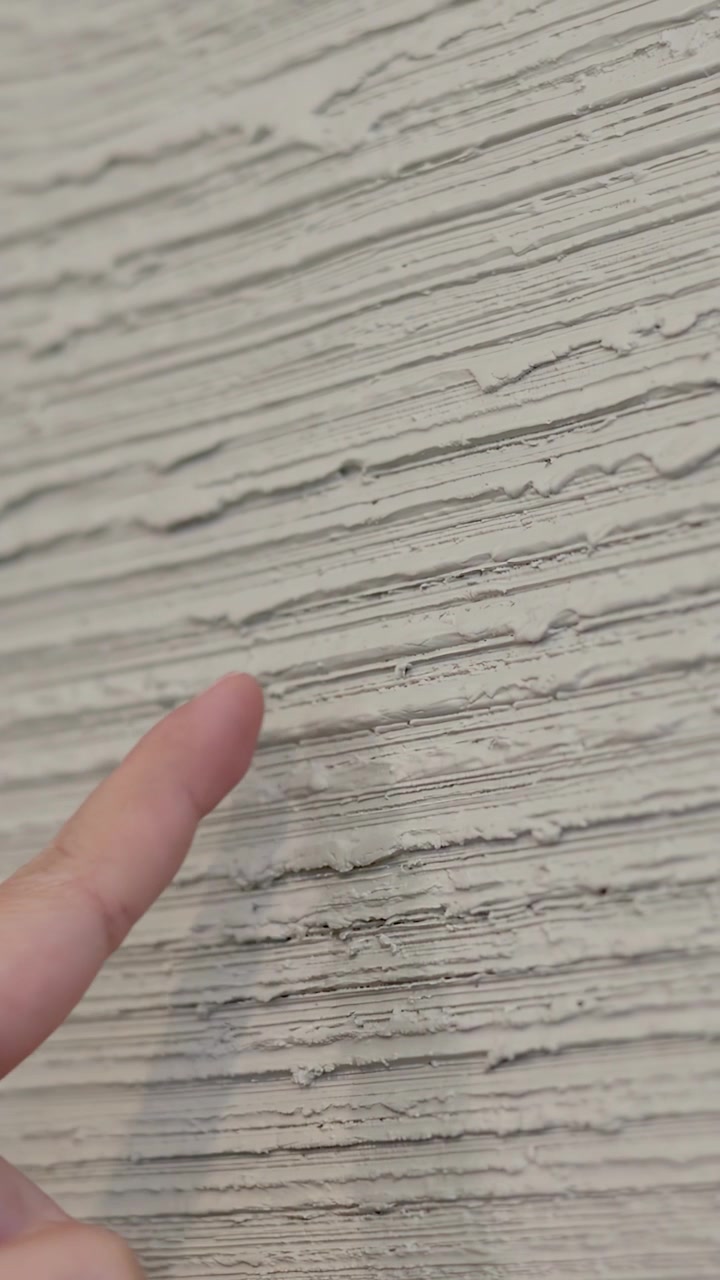 Person points at rough cement wall texture. Close-up shot with soft lighting and shallow focus.