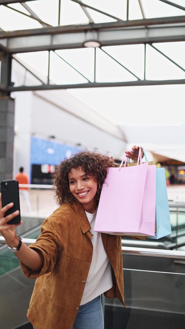 Giovane donna felice che scatta un selfie con borse della spesa al centro commerciale