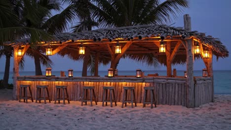 wooden beach bar with hanging lanterns illuminating the counter and stools on a sandy beach at dusk, creating a serene and inviting atmosphere