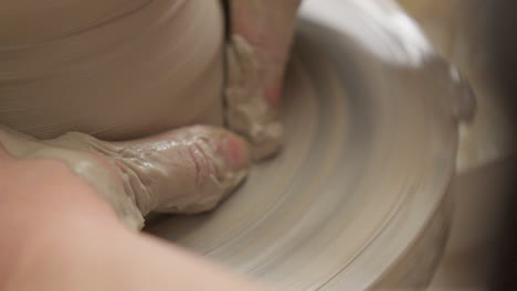Close up skilled artisan smoothing out the walls of a vase delicately with her hands on the potters wheel