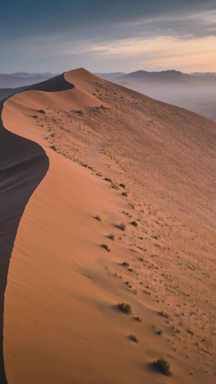 Video verticale: Drone che si alza e sfiora la cresta all'alba, rivelando i versanti delle dune illuminati dal sole e in ombra