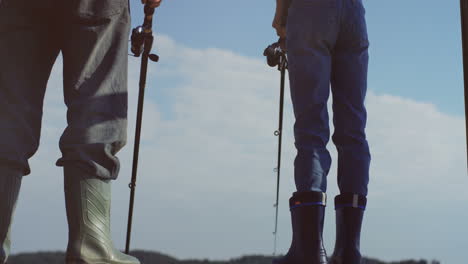 Camera-moving-from-feet-to-head-of-the-old-fisherman-with-his-small-grandson-standing-with-rods-in-hands-at-the-lake