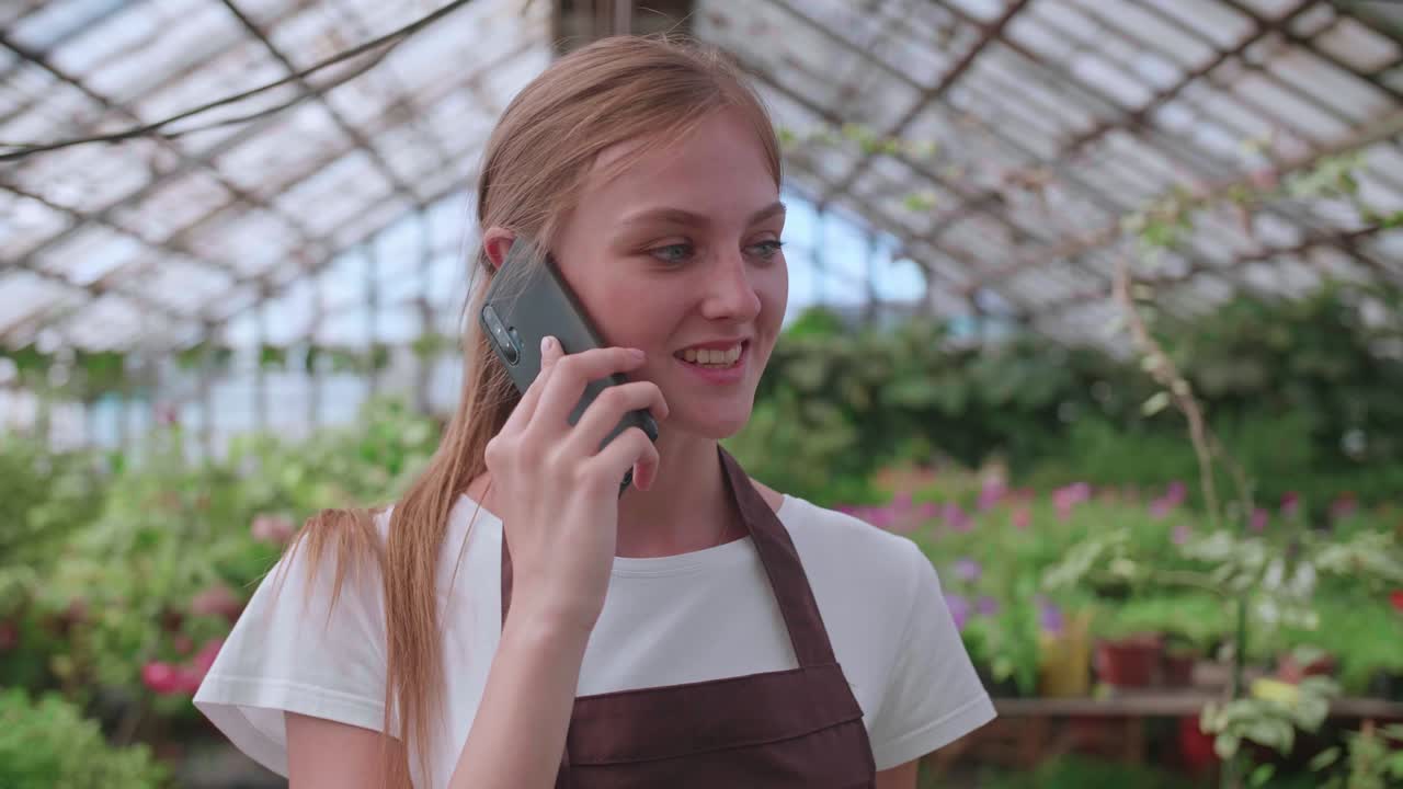 jovem trabalhadora de viveiro e estufa de flores fala com um cliente ao telefone