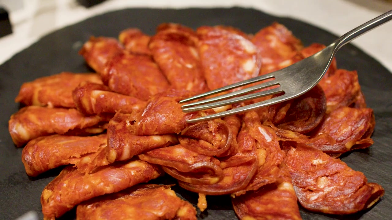 Gaffel plukker opp skivet chorizopølse fra en skiferplate