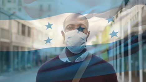 Animation-of-flag-of-honduras-waving-over-african-american-man-wearing-face-mask-in-city-street
