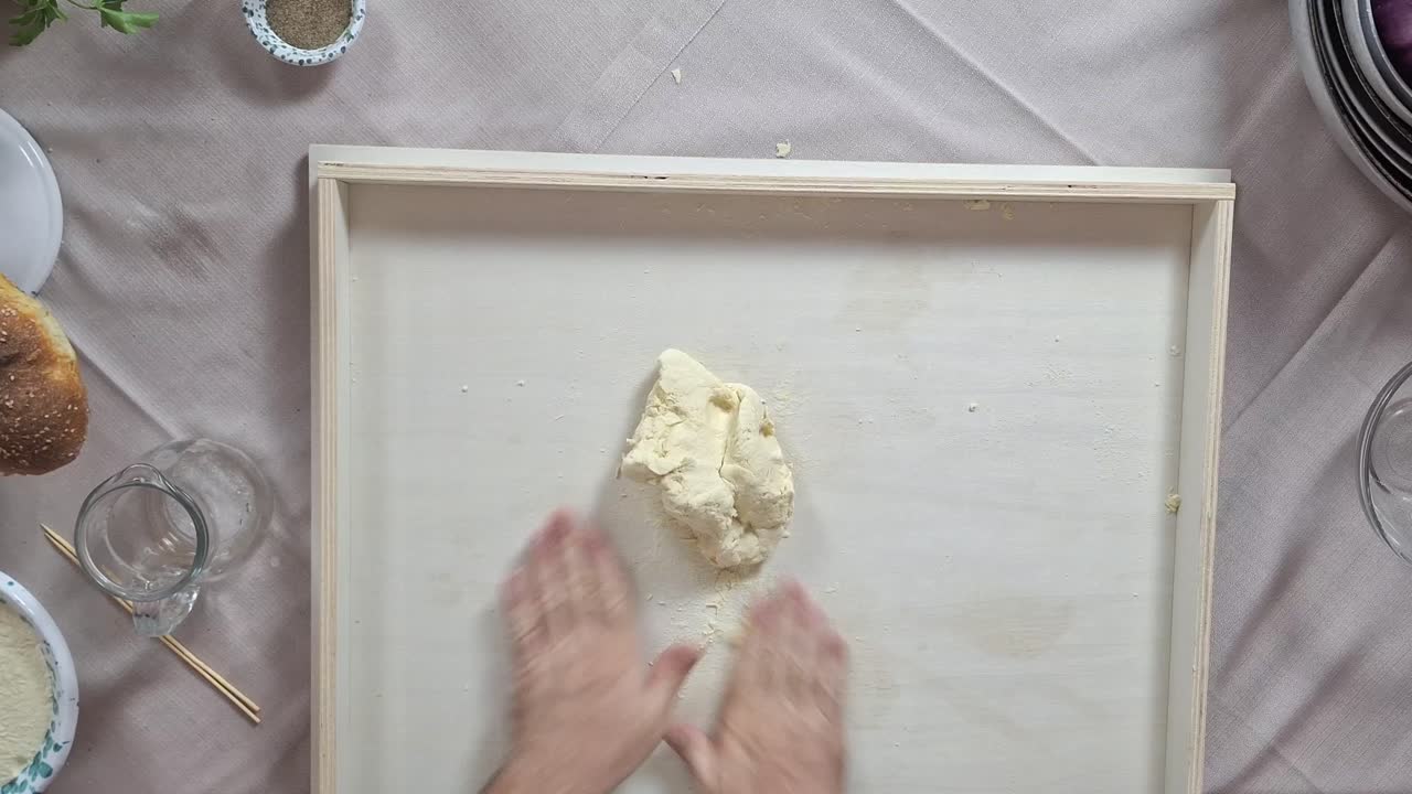 Top down overview of chef kneading handmade busiate pasta dough ball on prep surface