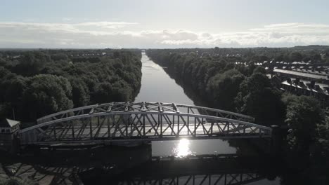 Ascending-tilt-down-above-scenic-old-fashioned-steel-arched-traffic-footbridge-over-Manchester-ship-canal-at-sunrise