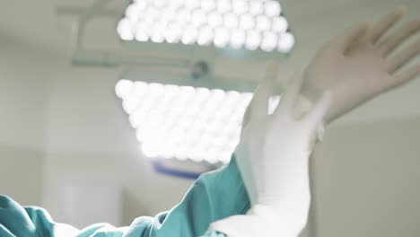 African-american-female-doctor-wearing-gloves-in-hospital-operating-room,-slow-motion