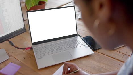 mujer de negocios afroamericana usando una computadora portátil con espacio para copiar y tomando notas en la oficina, cámara lenta