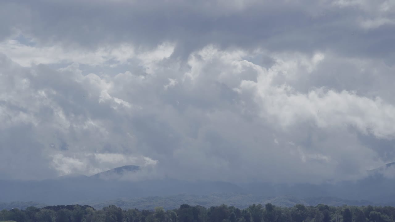 A dramatic landscape shot of heavy storm clouds moving over distant mountains and a forest line in the Posavje region of Slovenia