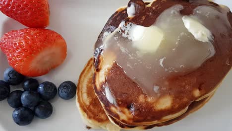 Over-top-zooming-into-pancakes-with-honey-butter-topping-and-strawberry-and-blueberries