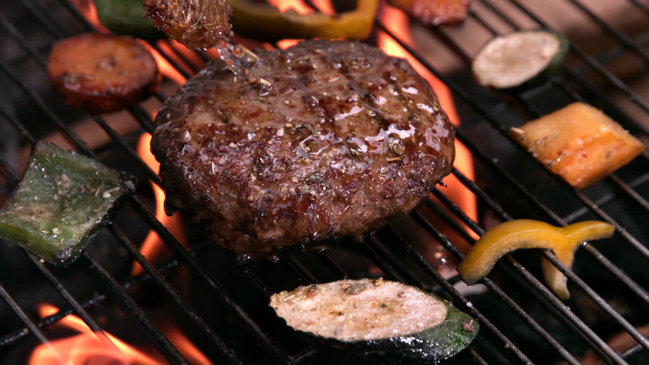 hamburguesa siendo cepillada con marinada en una barbacoa en llamas