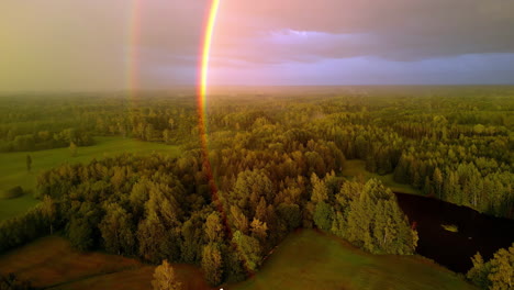 an aerial drone shot of a double rainbow over a forest landscape countryside in latvia