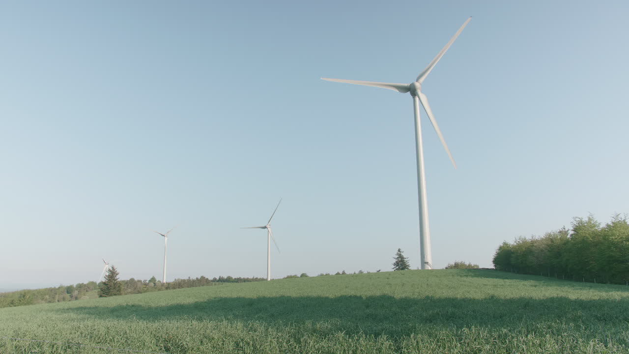 Documentary handheld shot of wind turbines turning along countryside rolling hill tops in the magic hour of afternoon sun light, gathering kinetic energy.