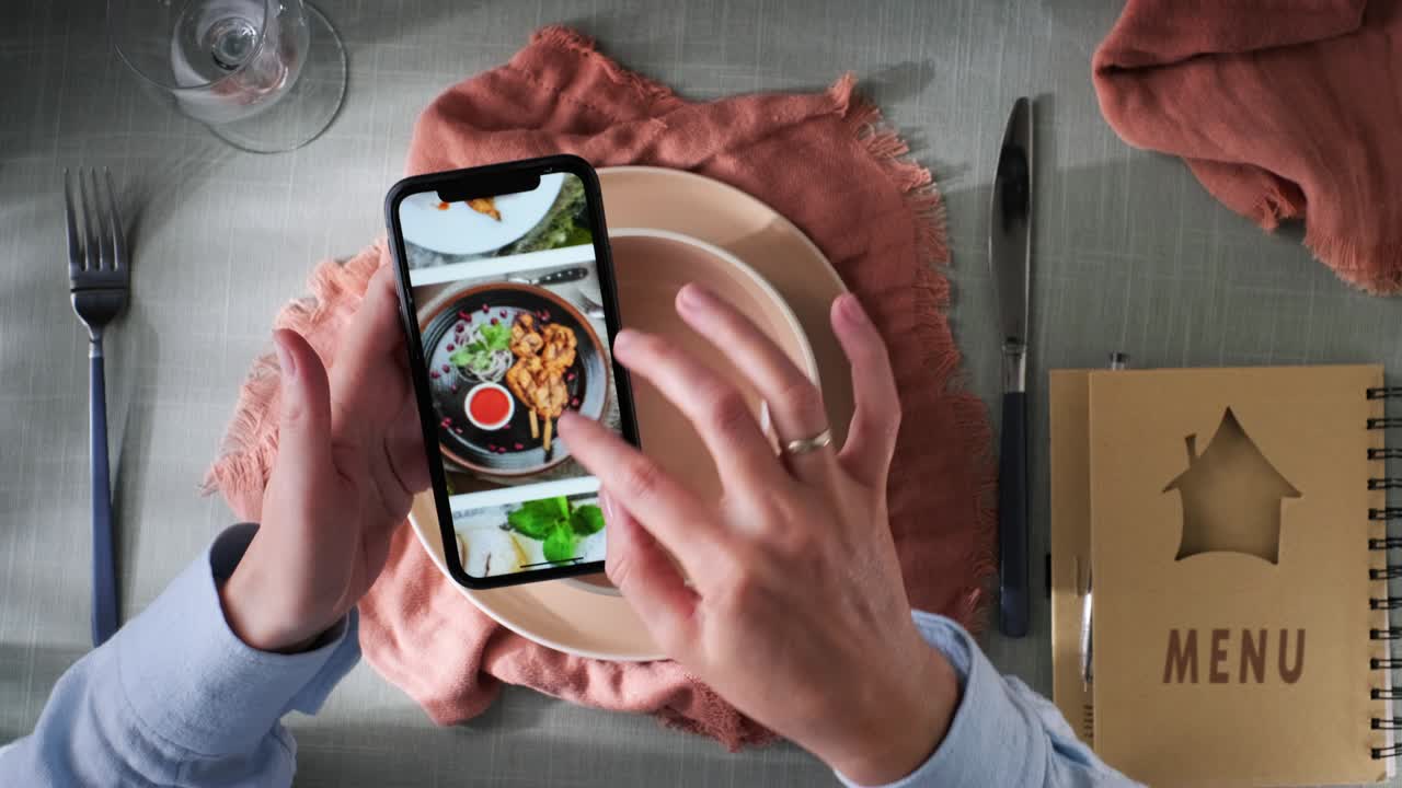 un visitante de un restaurante hojeando un menú de un restaurante en un teléfono móvil al lado es un menú en un cuaderno y platos con un cuchillo y un tenedor