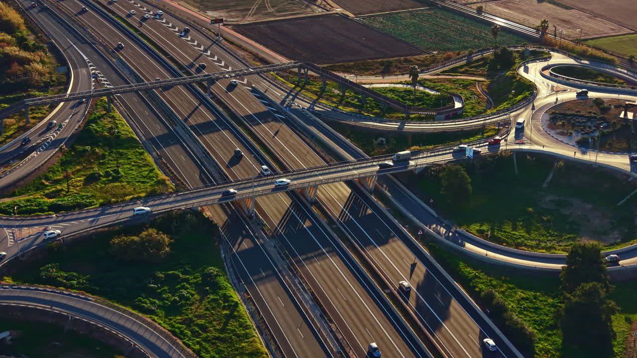 Il traffico scorre attraverso un trafficato incrocio autostradale in una zona rurale nel tardo pomeriggio, con veicoli che si muovono su più corsie