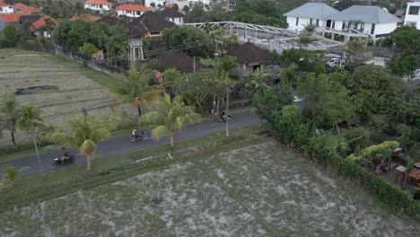 Aerial-orbits-two-cyclists-riding-on-small-road-in-rural-Cemagi,-Bali